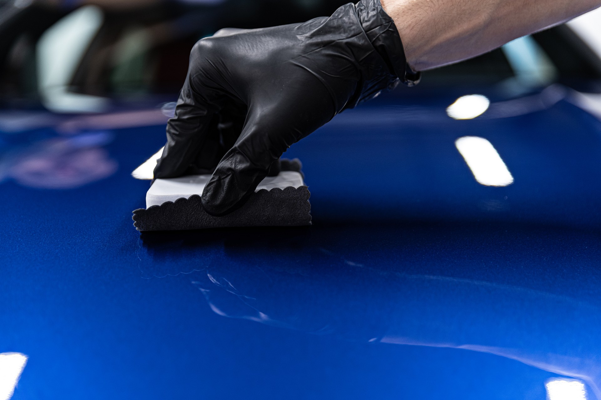 Man worker of car detailing studio applying ceramic coating on car paint with sponge applicator.