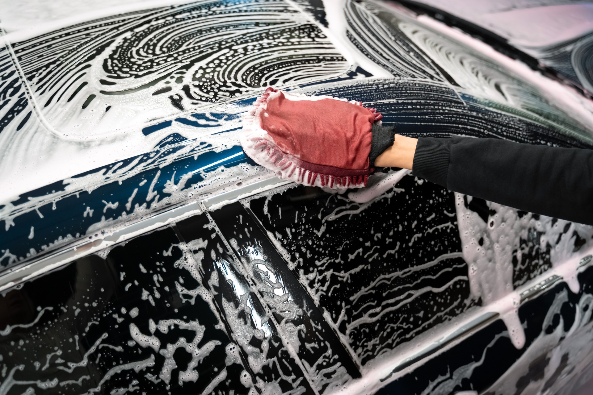 Professional car wash. Detailing worker washes the vehicle body with foam and rag